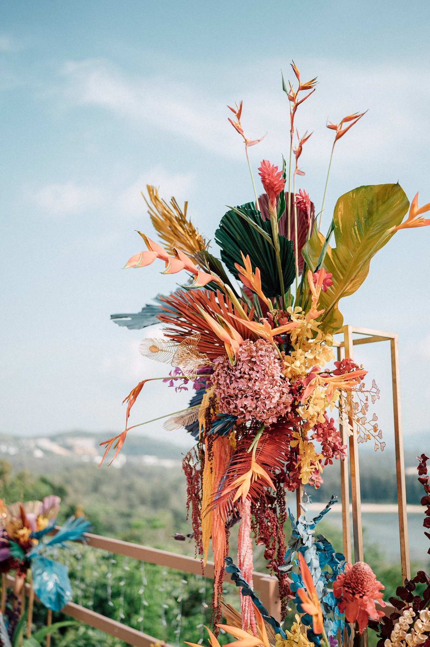 Warm-toned tropical pedestal arrangement with heliconia and palm leaf, film photography from a Sangeet at Anantara Layan
